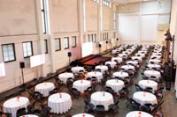 Pyöreät 120cm pöydät valkoisilla liinoilla ja istuimina mustat mukavat ja tukevat Jenkki-taittotuolit Iso määrä pyöreitä pöytiä valkoisilla pöytäliinoilla ja mustia Jenkki-taittotuoleja Kattilahallissa Helsingin Suvilahdessa