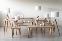 Useita eri kokoisia ja korkuisia puisia Saarni-pöytiä sekä jalkalamppuja valokuvausstudiossa