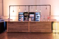 Kaksi puupintaista tapahtumatiskiä ketjutettuna baaritiskiksi, kuvassa myös PD-telinettä, koristevaloja ja jääkaappeja