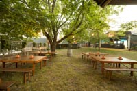 Rustiikkisia penkkipöytäsettejä puutarhamaisessa miljöössä kesäillassa Tuska Festivaaleilla Helsingin Suvilahdessa kesällä 2024 Rustiikkisia penkkipöytäsettejä puutarhamaisessa miljöössä kesäillassa