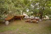 Rustiikkisia penkkipöytäsettejä puutarhamaisessa miljöössä kesäillassa Tuska Festivaaleilla Helsingin Suvilahdessa kesällä 2024 Rustiikkisia penkkipöytäsettejä puutarhamaisessa miljöössä kesäillassa