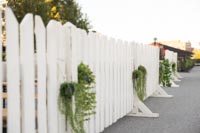 Valkoista puuaitaa mihin on ripustettu tekoviherkasveja