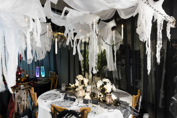 Pyöreä pöytä sekä Camelot ja Greta -puutuoleja somistettuna kauhu-/Halloween-illalliselle. PD-telineistä roikkuu joukko haamuja ja LED-kynttilöitä.