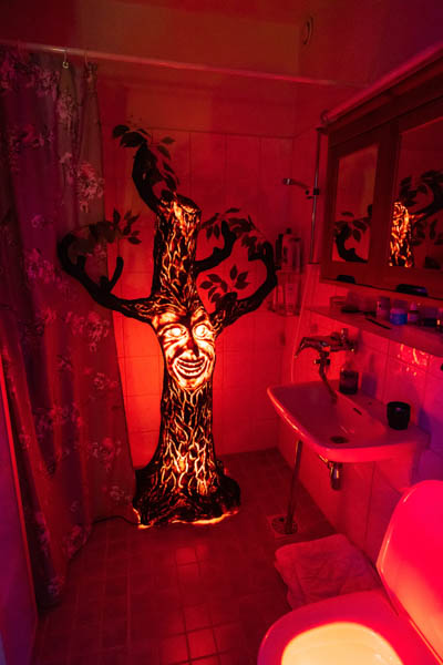 Punaisella valaistu kauhuaiheinen tekopuunrunko missä on henkilön naama. Kuva otettu yksityishenkilön kylpyhuoneessa Halloween-juhlissa