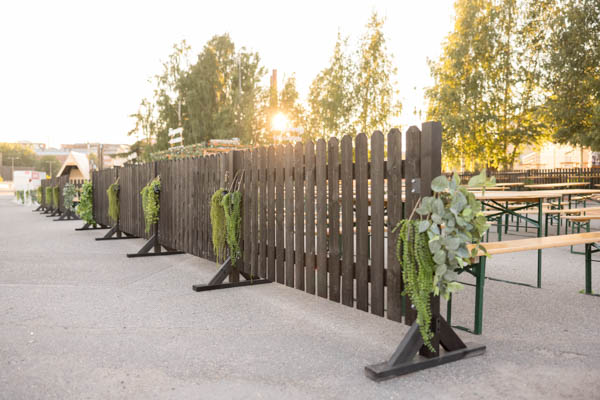 Mustaa puuaitaa Tuska-festivaaleilla somisettuna yksinkertaisin ripustetuin tekoviherkasvein. Kuva on otettu rakennusvaiheessa kauniissa kesäillassa.