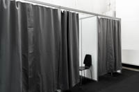 Useampi pukukoppi ketjutettuna isoksi kokonaisuudeksi Pukukoppeja rivinä mustalla verholla. Yhden kopin verho on raollaan ja sen sisällä näkyy pinottava vuokratuoli